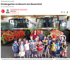 Eine Kindergruppe und zwei Erwachsene posieren vor zwei großen Claas Mähdreschern in einer Maschinenhalle.