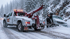 Towing Corona snow recovery service winching a stranded car from a snow-covered roadside during winter conditions.