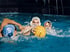 Drei Wasserballspieler kämpfen um einen gelben Ball im Wasser.