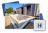 Ein Betonpool im Rohbau vor einem modernen Holzhaus mit einem gelben Bagger im Hintergrund und einem blauen H-Logo.
