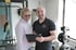 Ein Personal Trainer und eine Kundin lächeln in einem Fitnessstudio, er hält ein Klemmbrett.