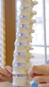 Ein Modell der menschlichen Wirbelsäule mit sichtbaren Bandscheiben und zwei Händen, die es berühren.