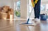 Reinigungskraft wischt Laminatboden in heller Wohnung mit Umzugskartons im Hintergrund.