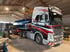 Ein weißer Volvo Schwerlast-LKW mit rotem Dekor wird in einer Lagerhalle mit blauen Metallteilen beladen.