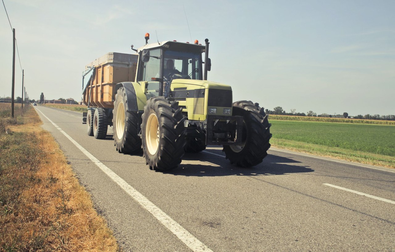 A tractor hauling a trailer along a rural asphalt road, the farm equipment on the road that Hanford, California drivers share two-lane routes with