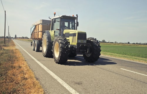 A tractor hauling a trailer along a rural asphalt road, the farm equipment on the road that Hanford, California drivers share two-lane routes with