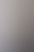 Eine lächelnde Frau mit braunen Haaren in einem weißen T-Shirt und Jeans sitzt vor einer grauen Wand.