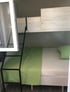Etagenbett mit weißer Bettwäsche, grüner Decke und Kissen, schwarzer Leiter und Holzpaneelen.