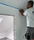 Handwerker klebt die Kante an einer frisch verkleideten Decke ab, daneben der Durchgang zur Dachschräge