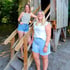 Zwei Frauen in Shorts und T-Shirts stehen auf einer Holztreppe vor einem Baumhaus.