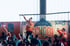 Ein Mann in Orange tanzt auf einer Bühne vor einem Banner mit der Aufschrift „MOVE IN SCHOOL“; Kinder schauen zu.