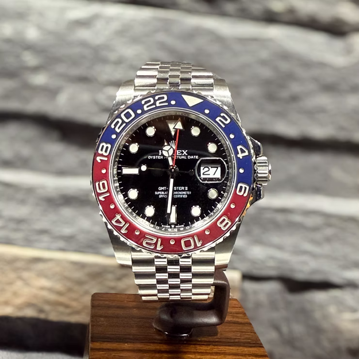 Eine Rolex GMT-Master II Uhr mit rot-blauer Lünette und Datumsanzeige 27 auf einem Holzständer.