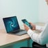 Person am Schreibtisch hält ein Smartphone neben einem Laptop, beide Geräte zeigen eine Benutzeroberfläche mit Wirbel-Design.