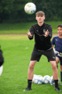 Ein junger Fußballspieler in schwarzen Sportkleidung fängt einen Fußball auf einem grünen Rasen.