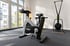 Ein helles Fitnessstudio mit einem Technogym Indoor-Bike und einem Ski-Ergometer vor einem großen Fenster.