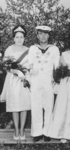 Schwarz-weiß-Foto einer jungen Frau in Kleid und Tiara, die neben einem Mann in Marineuniform steht.