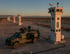 Militärfahrzeug neben einem Wachturm mit Kameras und Antennen; eine Reihe ähnlicher Türme erstreckt sich in die Ferne.