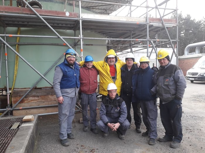 Montageteam mit Schutzhelmen vor einem eingerüsteten Behälter