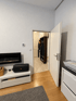 Wohnzimmer mit Elektrokamin, weißem Lowboard und Blick durch eine offene Tür in einen Flur mit Garderobe.