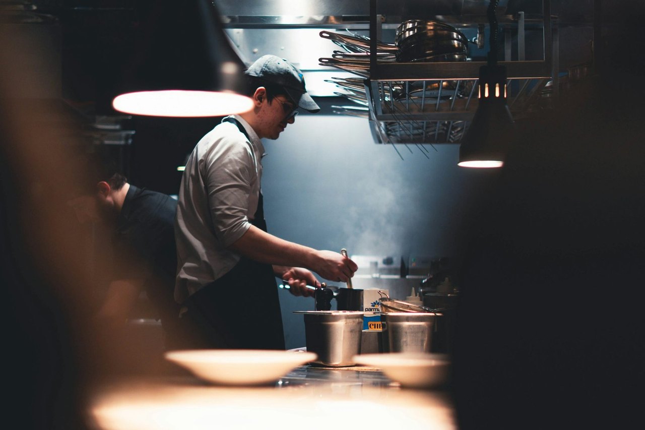 Koch arbeitet am Herd in einer dunklen Restaurantküche unter Hängelampen