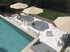 Terrasse am Pool mit weißer Lounge-Möbeln und beigen Sonnenschirmen unter blauem Himmel.
