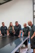 Das Team von Singer und Singer in dunklen Poloshirts begutachten gemeinsam eine Glasplatte an einem Arbeitstisch in einer Werkstatt.