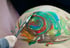 Bunter Pinsel malt kreative Formen auf den Babybauch – Bodypainting während der Schwangerschaft, fotografisch festgehalten.