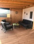 Geräumige Terrasse mit Holzboden, großem Esstisch, 8 Stühlen und L-förmigem Sofa.