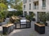 Moderne Außenküche mit Edelstahl-Gasgrill, zwei Küchenwagen und langem Holztisch auf einer gepflasterten Terrasse.