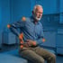 Man sits on an exam table, grimacing and holding his lower back, with red pain points targeted for trigger point injections.
