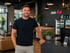 Lächelnder Mann in schwarzem T-Shirt vor der Theke eines "club vital" Fitnessstudios.