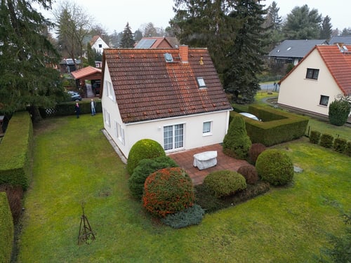 Ein Einfamilienhaus mit rotem Ziegeldach, umgeben von einem grünen Garten mit Hecken und Büschen.