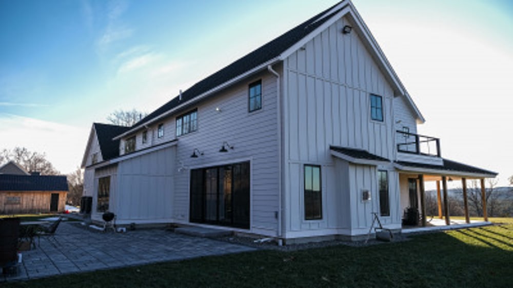 Back view of a farmhouse style home with front porch wrapping partially around.