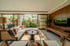 A modern living room with a long sectional sofa, wooden coffee table, large TV, and glass doors opening to a lush garden.
