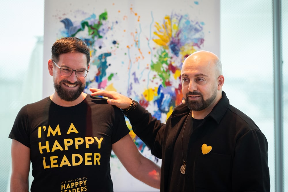 Ali Mahlodji legt Matthias Lechner im Shirt „I’m a Happpy Leader“ die Hand auf die Schulter