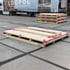 Helle Individuelle Holzpalette konfiguriert auf einem grauen Betonboden mit dunklen Fugen.