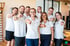 Das LANDphysio-Team in weißen Poloshirts lächelt und zeigt in der Physiotherapiepraxis in Lauchdorf im Allgäu auf die Kamera.