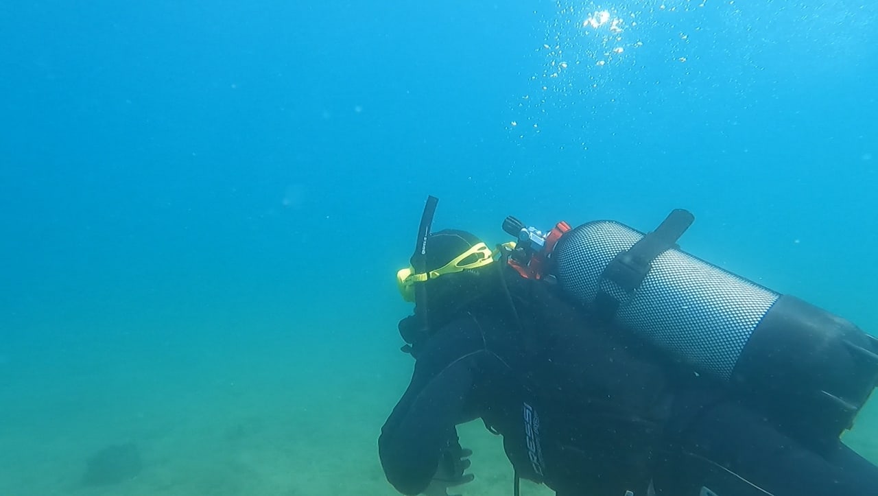 A scuba diver with tank and mask gliding through clear blue water