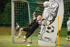 Ein junger Torwart im schwarzen Trikot springt nach einem Fußball, der über eine aufblasbare Puppe fliegt.