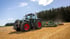 Grüner Fendt-Traktor mit roten Felgen zieht landwirtschaftliche Geräte über ein goldenes Feld unter blauem Himmel.