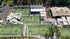 Aerial view of multiple green padel tennis courts with white nets, surrounded by buildings, trees, and shaded seating areas.