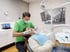 Zahnarzt in grüner Kleidung und Maske untersucht eine Patientin auf einem Zahnarztstuhl.