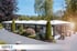 Eine lange, moderne Glasveranda mit weißem Dach und schwarzem Rahmen steht in einer grünen Landschaft.