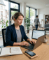 Eine Social Media Managerin aus Speyer tippt an einem Holztisch auf einem Laptop, daneben liegen Notizbuch, Stift und Smartphone.