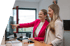 Zwei lächelnde Kolleginnen im Büro betrachten gemeinsam einen Monitor, während eine Frau auf den Bildschirm deutet.