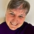 Woman with short gray hair and a purple shirt smiling at the camera.