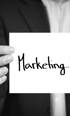 Eine Hand hält ein weißes Blatt Papier mit dem handgeschriebenen Wort „Marketing...“ in Schwarz.