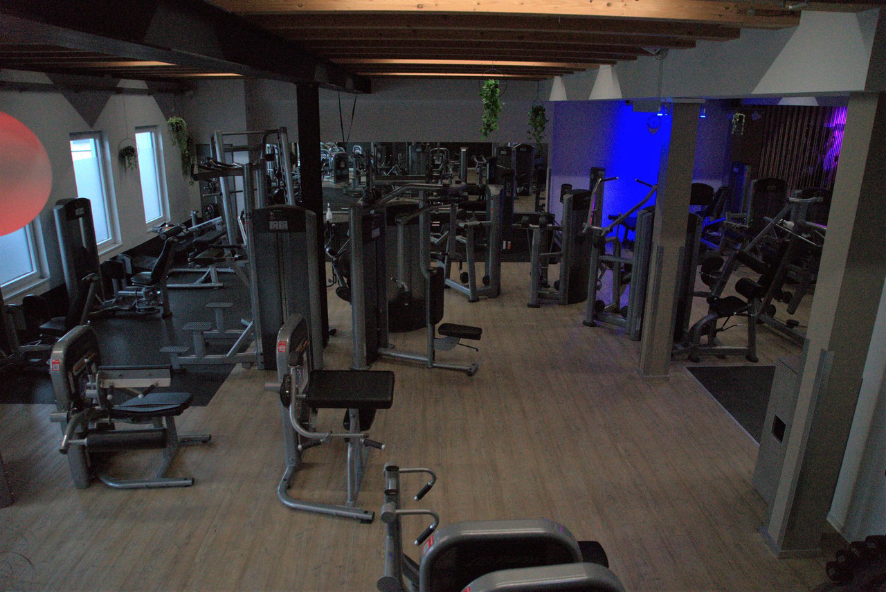 Fitnessstudio mit vielen Trainingsgeräten und blauer Beleuchtung.