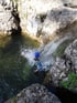 Person in Neoprenanzug und blauem Helm springt in einen natürlichen Wasserpool.