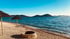 Feiner Kiestrand mit zwei Strohschirmen, einer Feuerstelle und ruhigem, blauem Meer unter klarem Himmel in Drage Kroatien-3V Holiday Resort